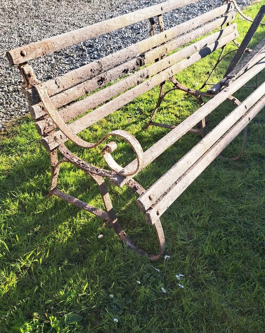 A rusted slatted metal garden bench on grass, before