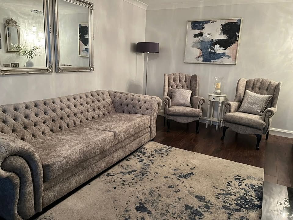 Room with a tufted sofa, two armchairs, side table, floor lamp, wall mirrors, abstract painting and patterned rug