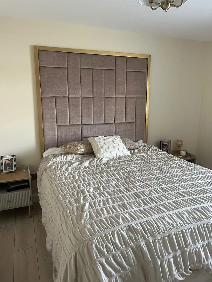 Bed with panelled fabric headboard, white ruched bedding, pillows and bedside tables in a beige room