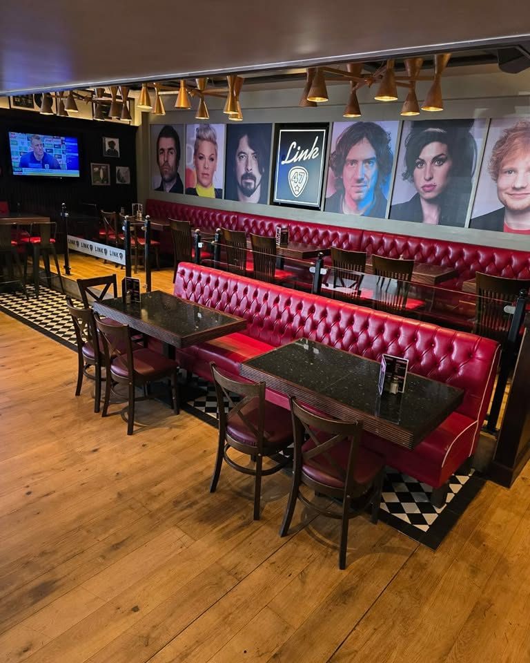 Restaurant seating area with red tufted booths, tables, chairs, pendant lights and portrait posters on the wall